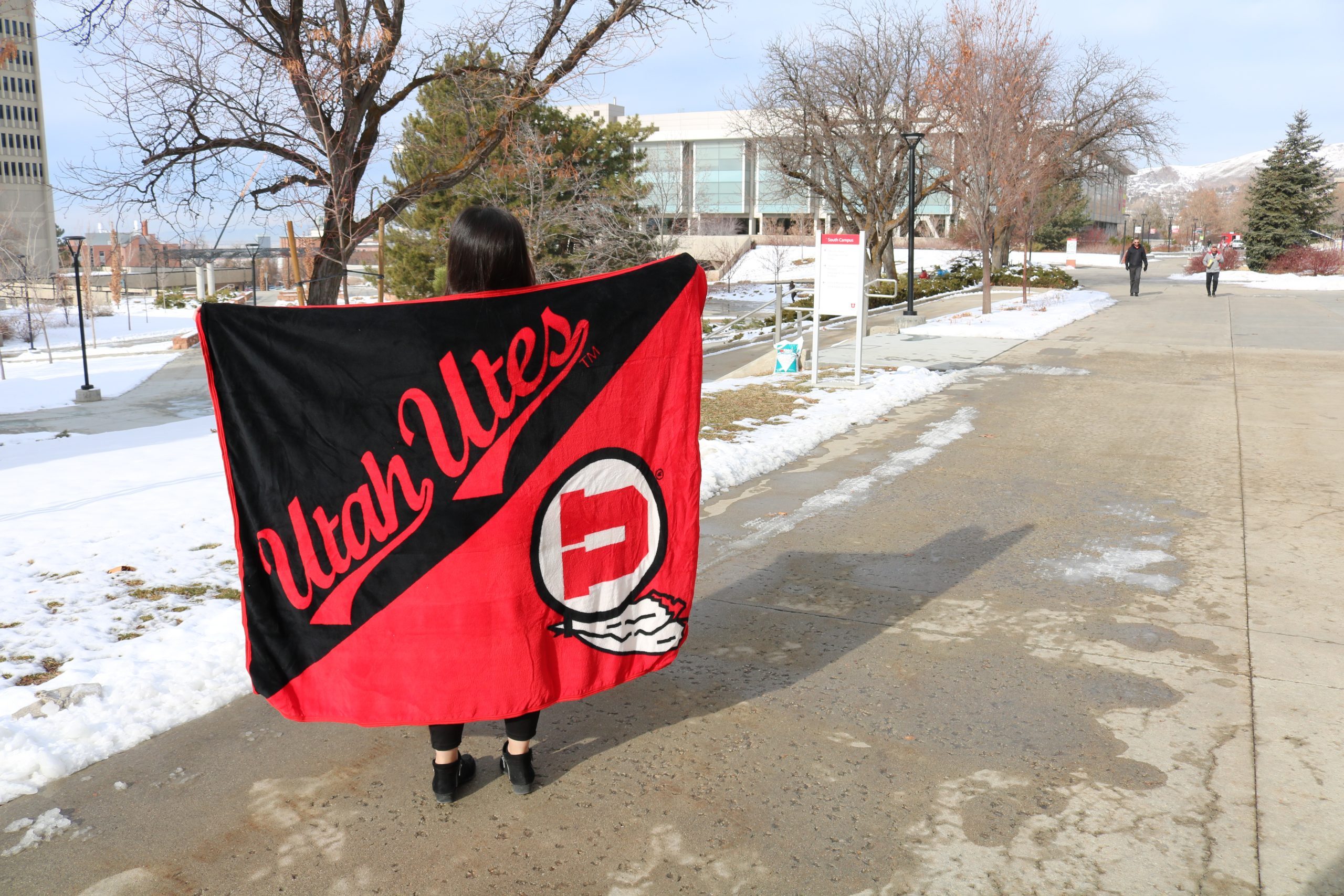 Student holds plush U-branded blanket on campus walkway